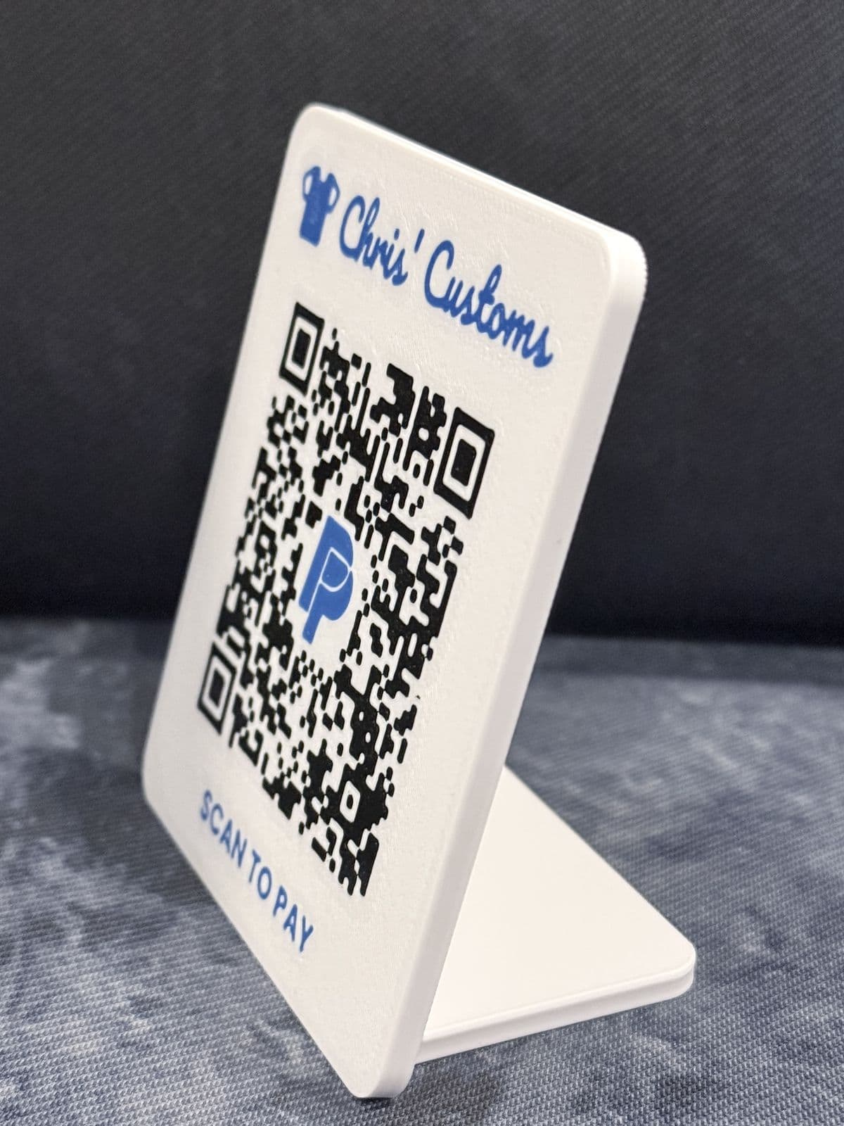 A white counter stand with a blue Chris' Customs script logo, a black QR code with a blue center logo, and Scan to Pay along the bottom